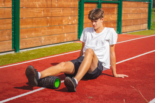 一个有着健壮体格的棕色头发的男孩坐在一个健壮的椭圆形椅子上，用泡沫滚轮按摩他的肌肉，以便更好地恢复。运动后图片下载