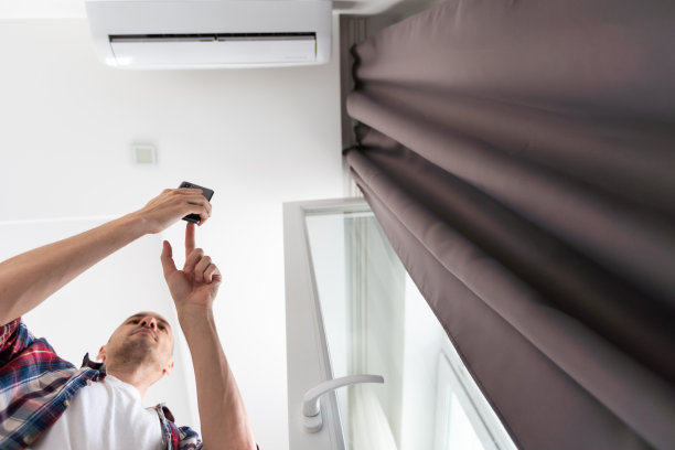 全身青年戴眼镜手持空调遥控器，放松，坐在沙发上，开关，设置舒适的温度在现代客厅，享受新鲜空气图片下载