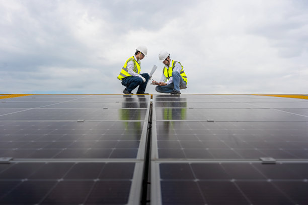 图为，年轻的亚洲工程师正在讨论在工厂屋顶安装太阳能电池的计划，前景是安装在工厂屋顶上的太阳能电池板。图片下载