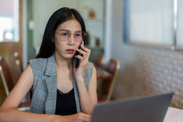 肖像，亚洲女性一边打电话一边在不错的咖啡馆面包店工作，但相反，工作压力大，坐在咨询或发泄压力，与人通电话，有严肃的态度。图片下载
