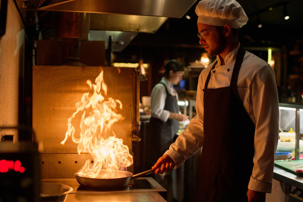 穿着制服的年轻厨师正在用大火煎锅准备新菜图片下载