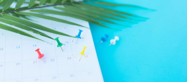 白色日历上的近距离俯视图，蓝色桌子背景上的图钉和热带树叶，在假期夏季概念中规划工作和生活平衡图片下载