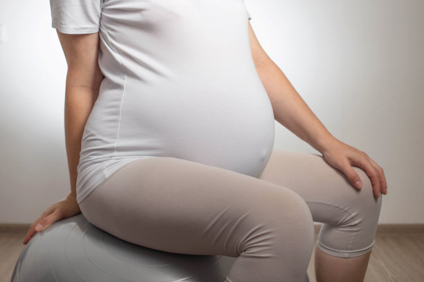 怀了孕的女孩拿着白底的健身球。怀孕期间做运动和健身的概念。健康和怀孕。图片下载