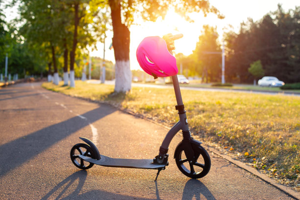 夏日夕阳的背景下，一辆戴着粉色头盔的现代摩托车停在一条小巷里。骑滑板车时的安全概念。文本复制空间图片下载