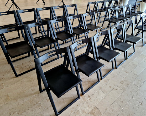 大厅里的塑料折叠椅。讲座听众或活动主持人。一排排挨着的长椅。黑色在米褐色的室内铺装上图片下载
