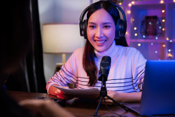 开朗美丽的亚洲女人戴着耳机，用笔记本电脑录播客。内容创造者概念。图片下载