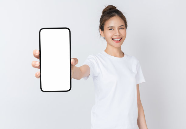 美丽的亚洲女人拿着空白屏幕的智能手机模型，在白色的背景上微笑。图片下载