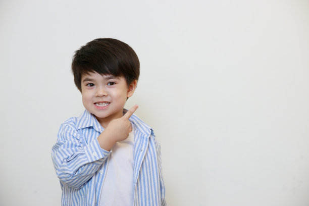 一个穿着得体的衬衫的小男孩正用他的手指着白色的背景。图片下载