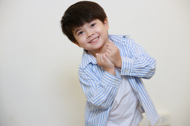 一个小男孩穿着礼貌的衬衫，在白色背景下摆出一个快乐的迷你心形姿势。图片下载