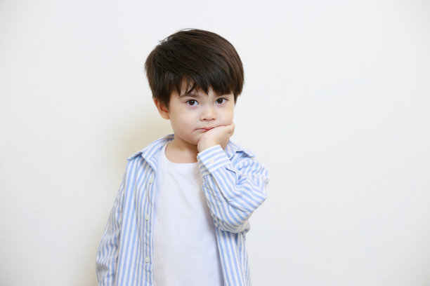 一个小男孩穿着彬彬有礼的衬衫，在白色的背景上用双手摆出一副若有所思的姿势图片下载