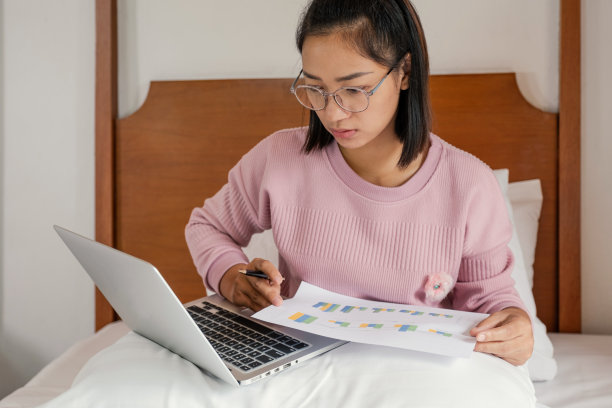 商务女记账员拿着笔，用笔记本电脑在床上做记帐纳税，在家办公的概念图片下载