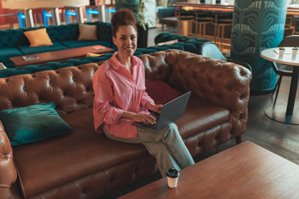 女自由职业者坐在沙发上，一边用笔记本电脑工作，一边看着摄像头图片下载