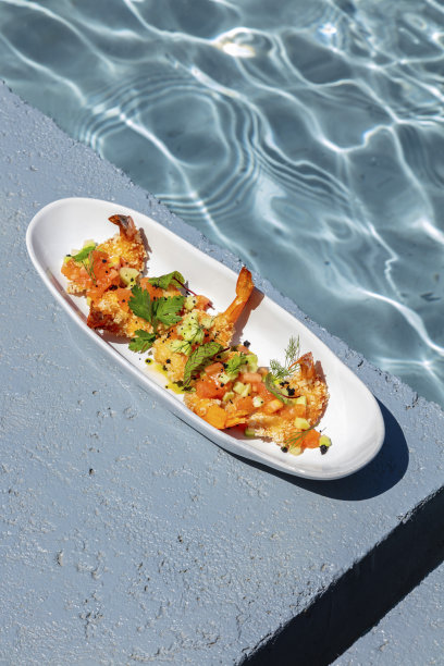 一个椭圆形的陶瓷盘子里放着天妇罗虾、蔬菜塔博列和香料。盘子立在水池附近的混凝土支架上。附近是一丛薰衣草。图片下载