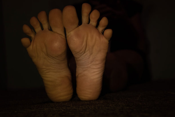 一个年轻的女孩坐在家里的地板上，女孩的脚在黑暗中特写，底部视图图片下载