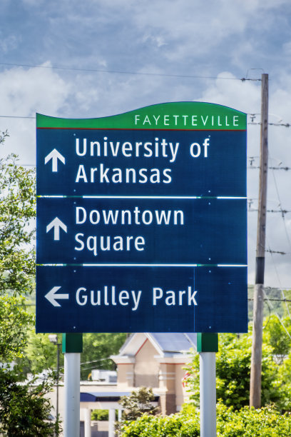 阿肯色大学、市中心广场和水沟公园的标志，背景是模糊的树木和建筑图片下载