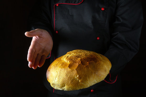面包师手里拿着刚烤好的小麦面包。黑色背景的广告位置。烤圆面包的概念图片下载
