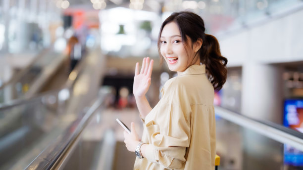 机场候机楼或现代火车站的年轻亚洲女性乘客。亚洲女通勤者在自动扶梯上带行李图片下载