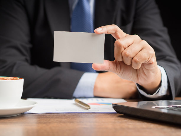西装革履的商人坐在办公室里，手里拿着一张名片模型图片下载