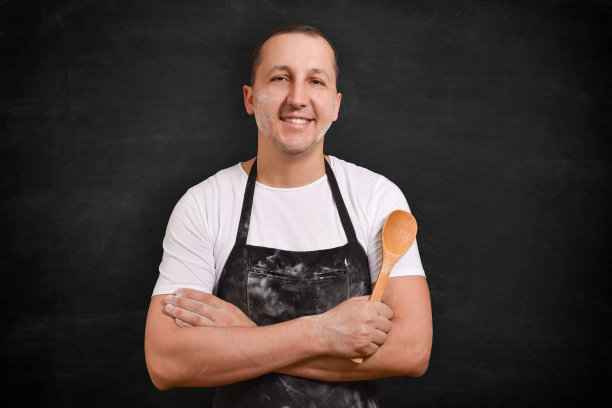 一个快乐的厨师或面包师的肖像在一个黑色的背景围裙看着相机。烹饪食物的概念。图片下载