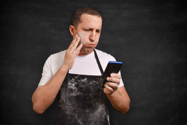 系着围裙的男面包师在黑色背景下打电话。烹饪与人的概念图片下载