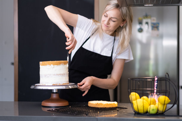 精力充沛的金发女人在厨房里把白奶油涂在烤蛋糕上图片下载