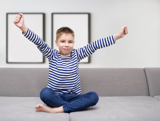 快乐的小男孩举起双手坐在沙发上图片下载