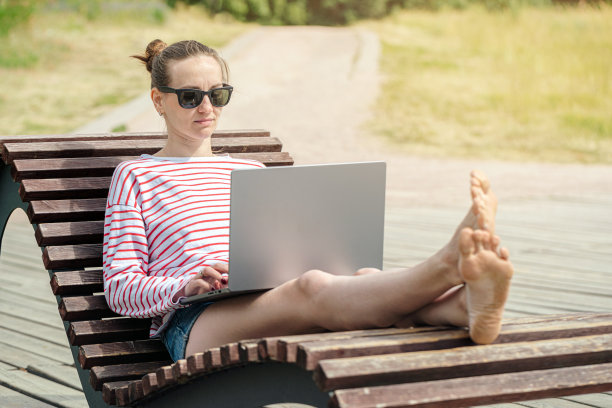 拿着笔记本电脑在公园户外工作的女交易员。图片下载