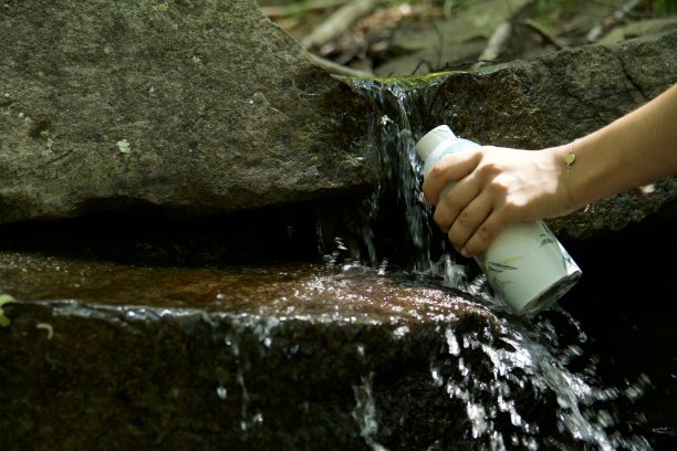 女孩在山泉边装水瓶图片下载