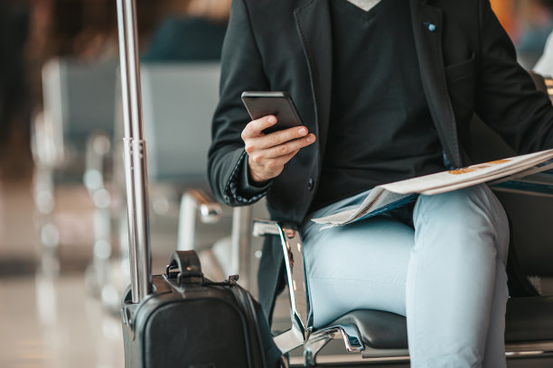 在机场候机室等待飞机的乘客。年轻人拿着智能手机在机场候机图片下载