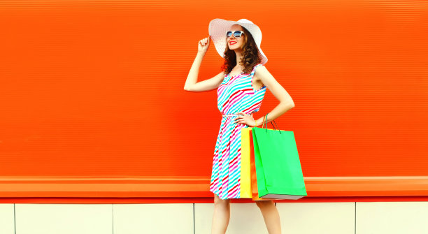 美丽快乐的年轻女子，带着五颜六色的购物袋，穿着裙子，戴着夏天的草帽图片下载