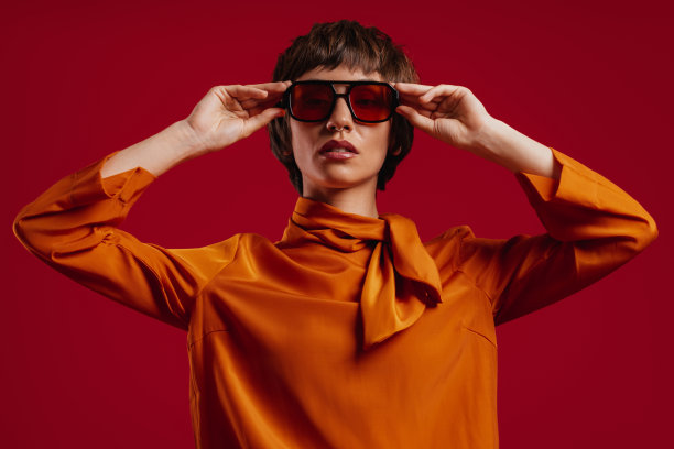 迷人的年轻短发女人在红色背景下调整她时髦的眼镜图片下载