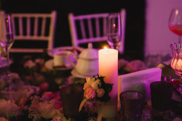 婚宴上的餐桌摆设。花卉组成与美丽的花朵和绿色植物，蜡烛，铺设和盘子在装饰的桌子。图片下载