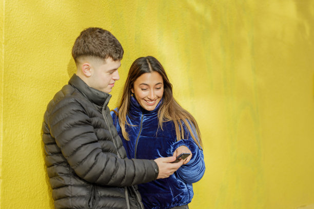 年轻夫妇看着手机，背景是带有复制空间的黄色墙壁。图片下载