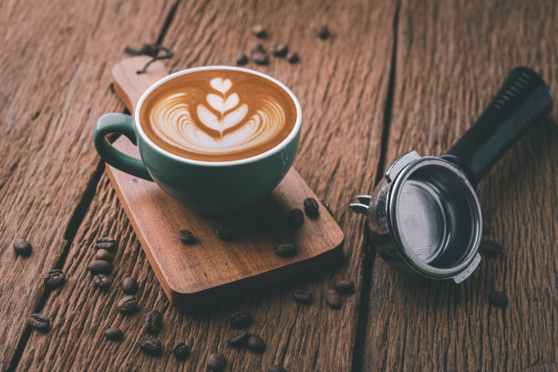 热拿铁咖啡上的拉花艺术。香气咖啡杯和咖啡豆放在木桌上。图片下载