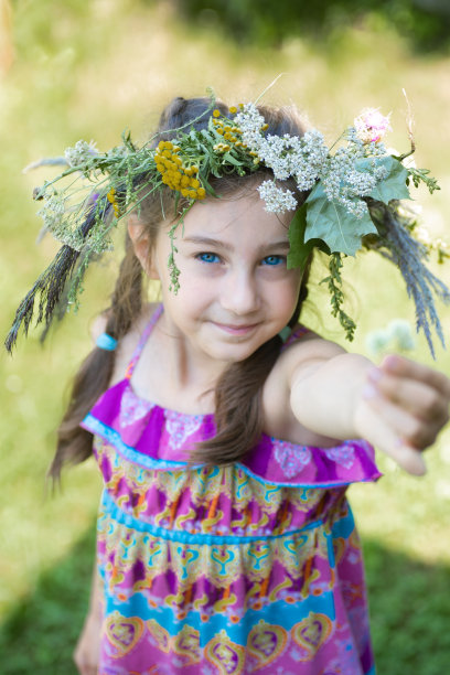 可爱的微笑小女孩与绿色背景花环。可爱的小孩在户外的肖像。仲夏。图片下载