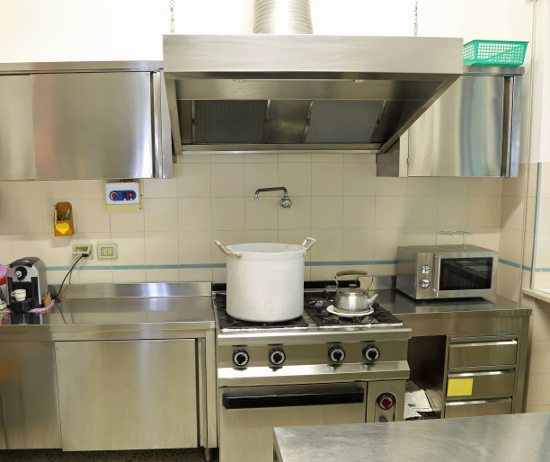 工业厨房，有一个大引擎盖和一个金属锅在炉子上图片下载