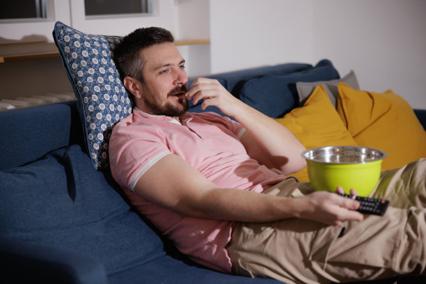 男人靠在沙发靠垫上，吃着爆米花，换着频道图片下载