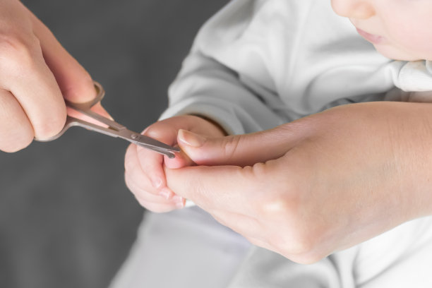 妈妈在家用特制的儿童剪刀在灰色的背景上给宝宝剪指甲。关闭了。新生儿修指甲图片下载
