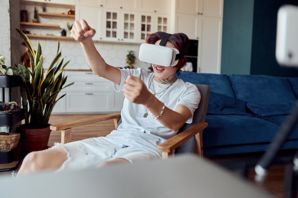 亚洲人坐在家里的扶手椅上，戴着VR头盔图片下载