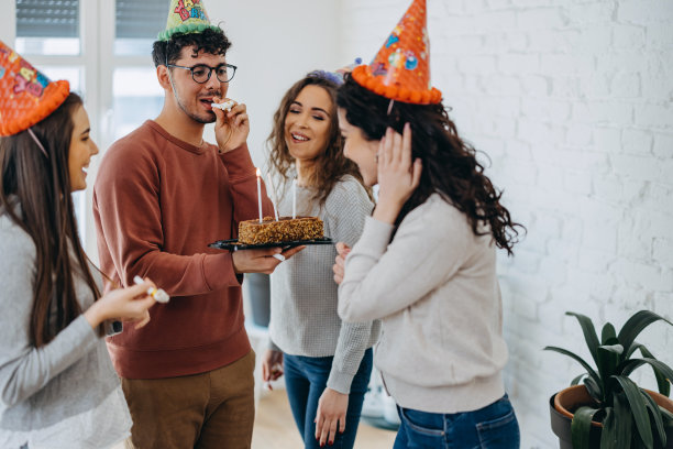年轻的朋友们为过生日的女人做惊喜，拿着点燃的蜡烛蛋糕，戴着派对帽，面带微笑图片下载