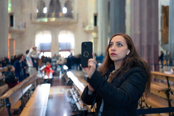 在西班牙巴塞罗那的观光旅行中，身着传统墨西哥服装，头戴耳机的年轻拉丁女游客在智能手机上拍摄历史建筑图片下载