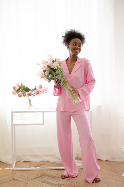 年轻快乐的非洲妇女穿着睡衣站在房间里，拿着花束，面带微笑。图片下载