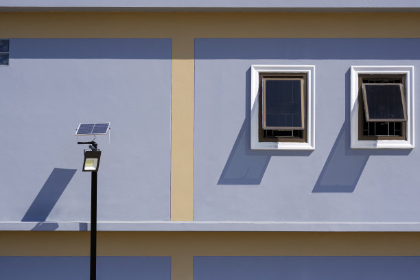 阳光和阴影的太阳能街灯柱与2玻璃窗在灰色和黄色的建筑墙壁图片下载