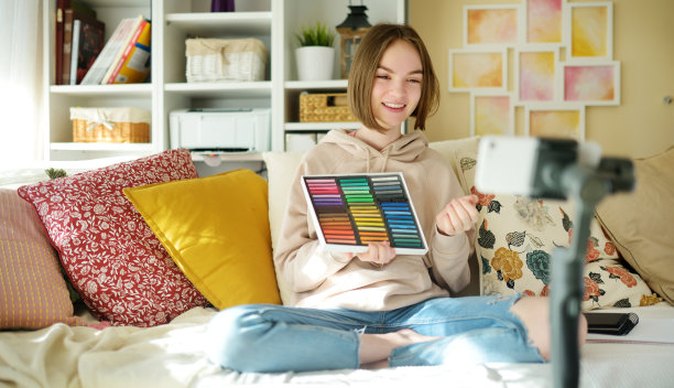 美丽的少女用她的智能手机录制视频博客。年轻的视频博主在家拍摄视频。青少年网红为她的社交媒体账户创建内容。图片下载