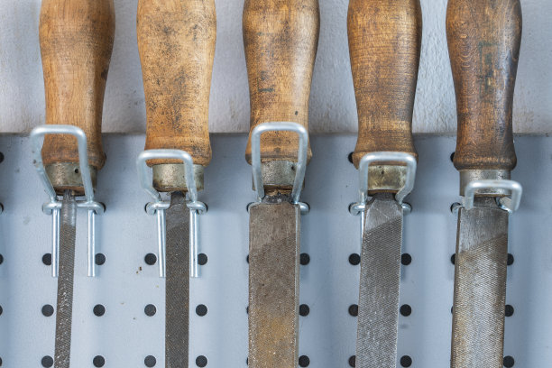 老式的木柄锉刀挂在钢墙上作为背景。一套用于手工打磨的锉刀和锉刀，特写。车间手工工具图片下载