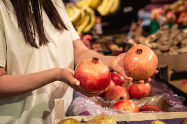 在商店或市场上，妇女手持石榴，近距离观看。图片下载
