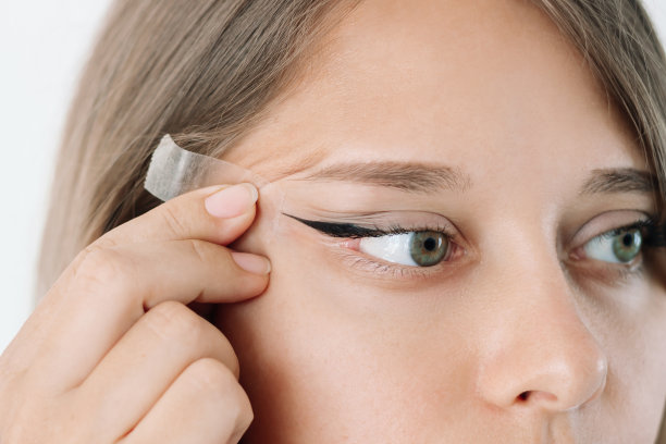 一个年轻的白人金发女人改变她的眼睛形状，用手把眼睑拉向一边图片下载