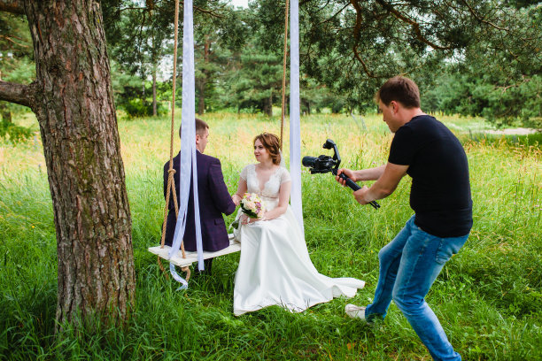 摄像师在松林中拍摄这对新婚夫妇在秋千上的镜头图片下载