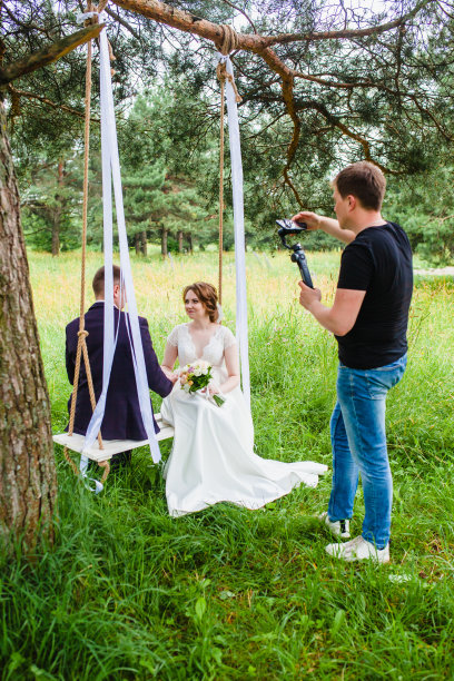 摄像师在松林中拍摄这对新婚夫妇在秋千上的镜头图片下载