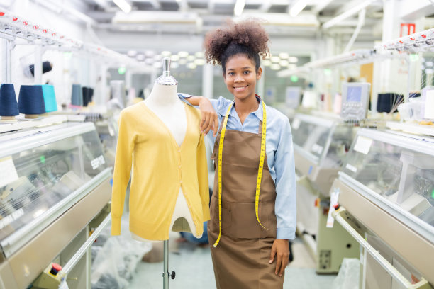 女设计师是女裁缝站在设计时装活动的人体模型旁边，带着卷尺，自信地微笑。有一台正在工作的缝纫机。图片下载